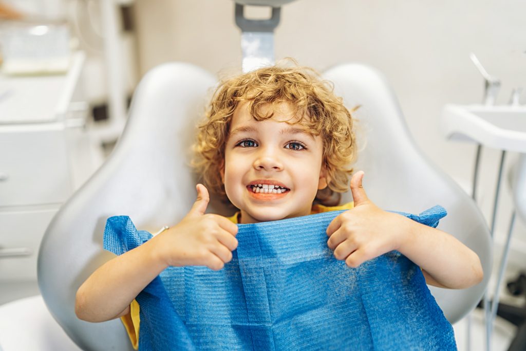 Child smiling in dental chair giving thumbs up